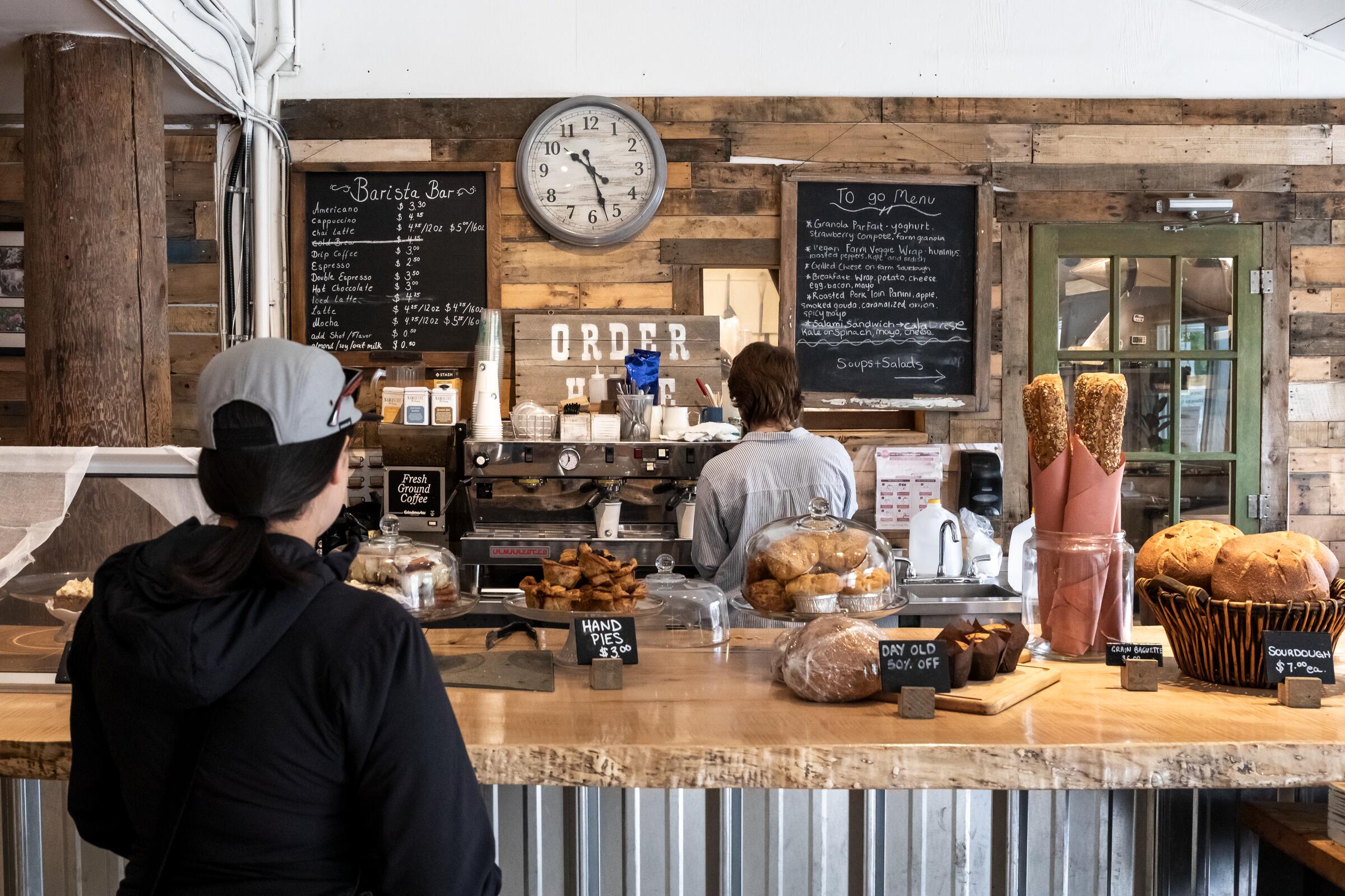 A customer waits at a Pemberton bakery counter lined with loaves, buns and chalkboard menus