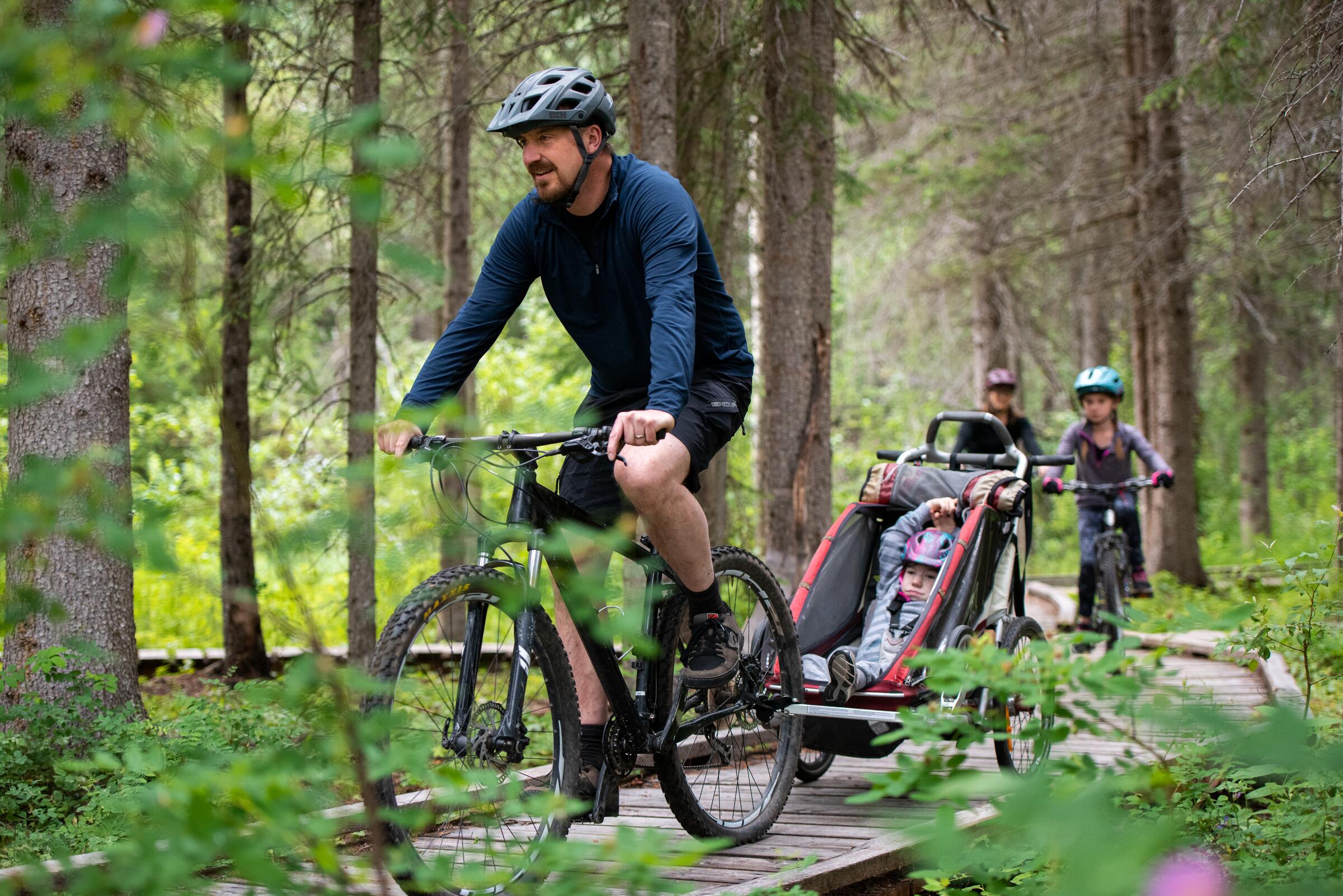 A family riding a forest boardwalk, a child in a bike trailer