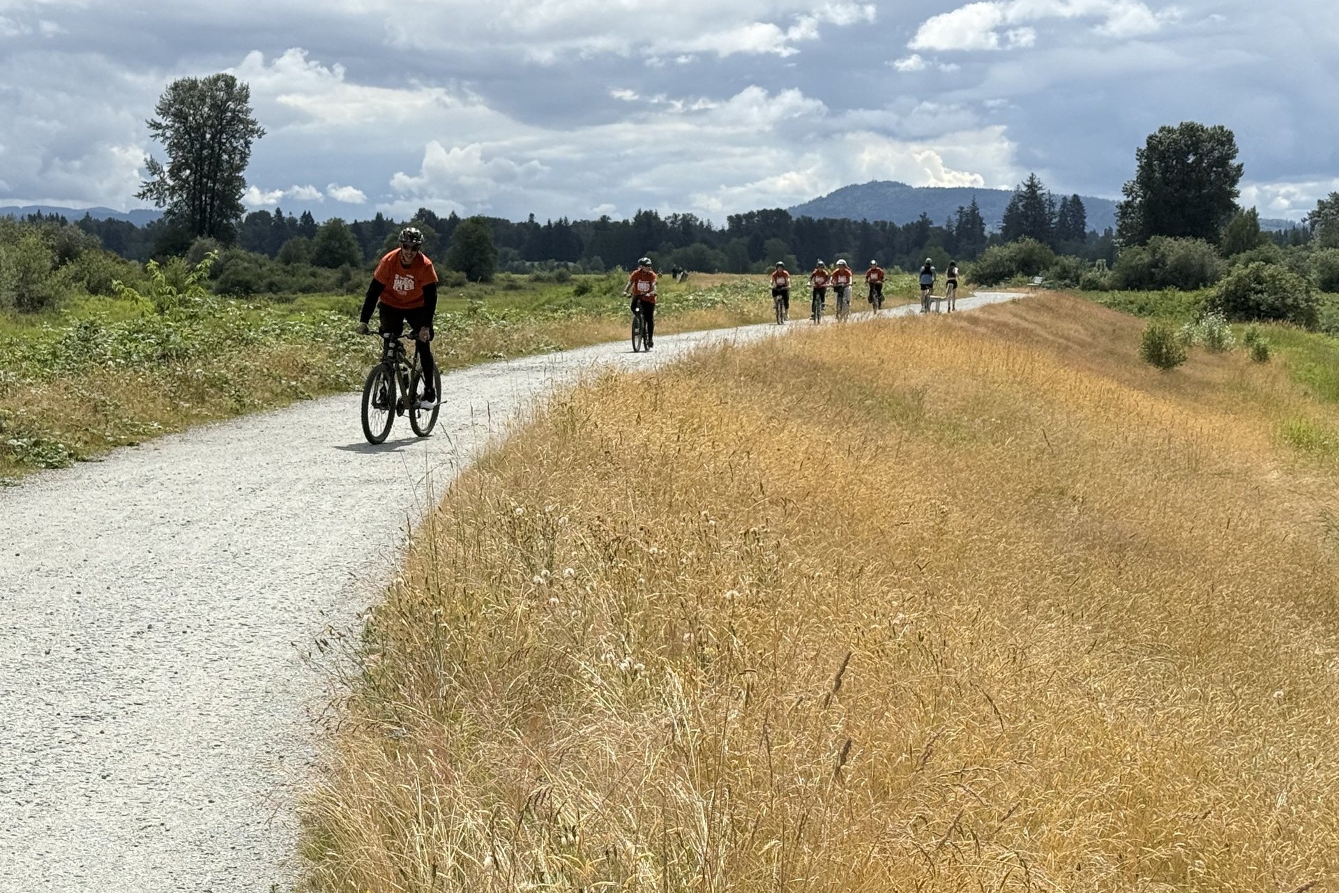 A group of riders on a gravel dyke trail under a big sky